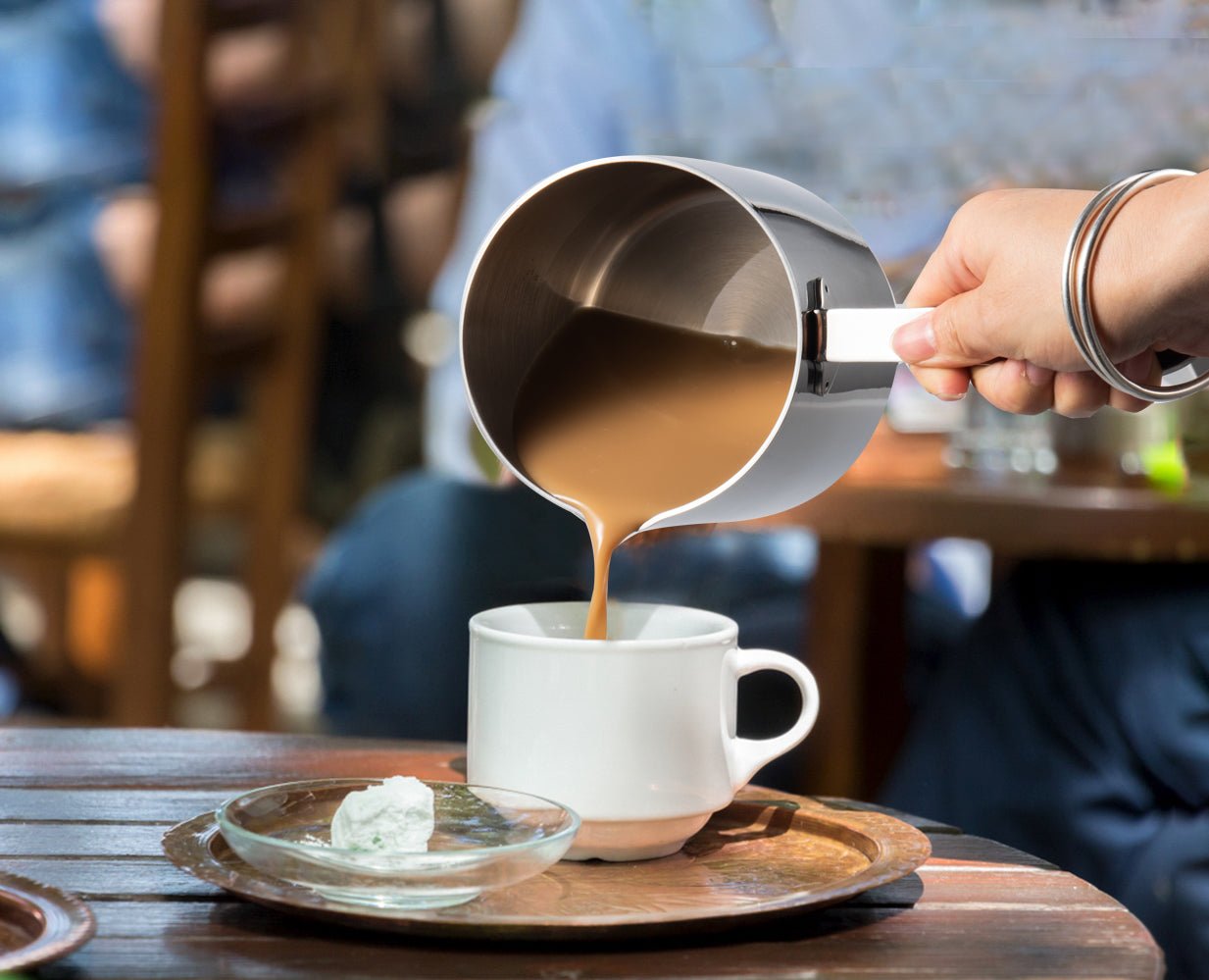 Small Stainless Steel Saucepan with Spout pouring hot coffee into a tea cup for serving
