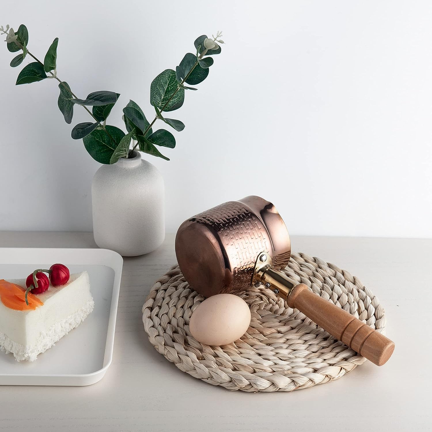 IMEEA Cezve with wooden handle placed on a table mat featuring a simple practical design