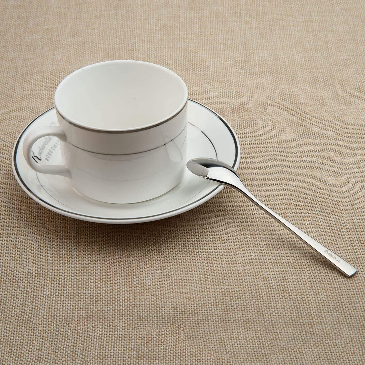 Small stainless steel espresso spoons placed in a tea cup saucer for coffee and tea serving