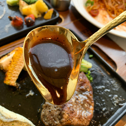 IMEEA gold stainless steel gravy ladle filled with black pepper sauce over steak