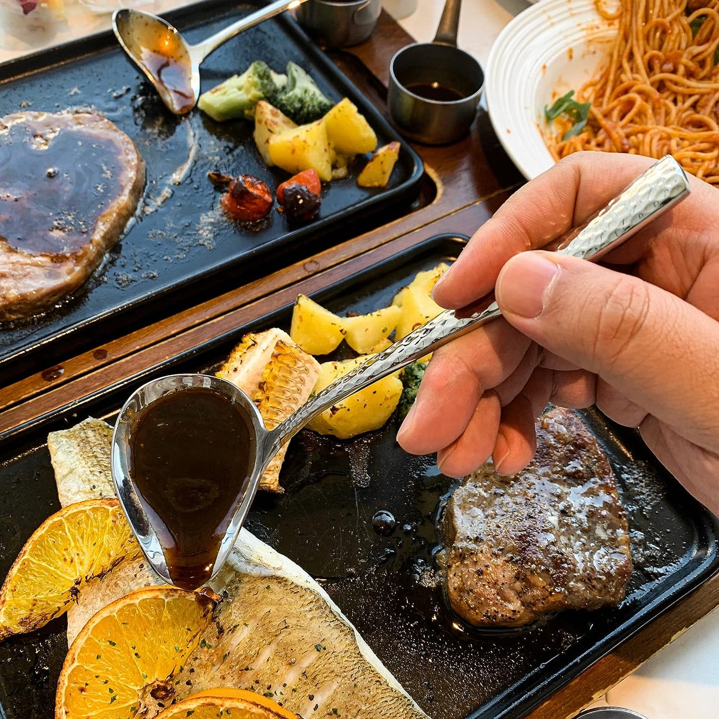 IMEEA stainless steel gravy ladle with pour spout being used to drizzle sauce over grilled fish on a serving tray
