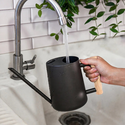 Stainless Steel Watering Can with Splash Guard Design and Wooden Handle filling water from a faucet