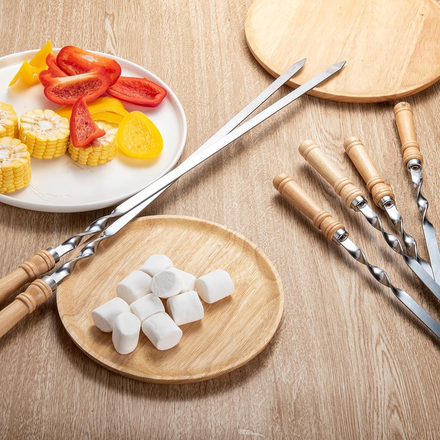 Large flat kabob skewers displayed on a table with fresh grilling ingredients for a BBQ preparation setup