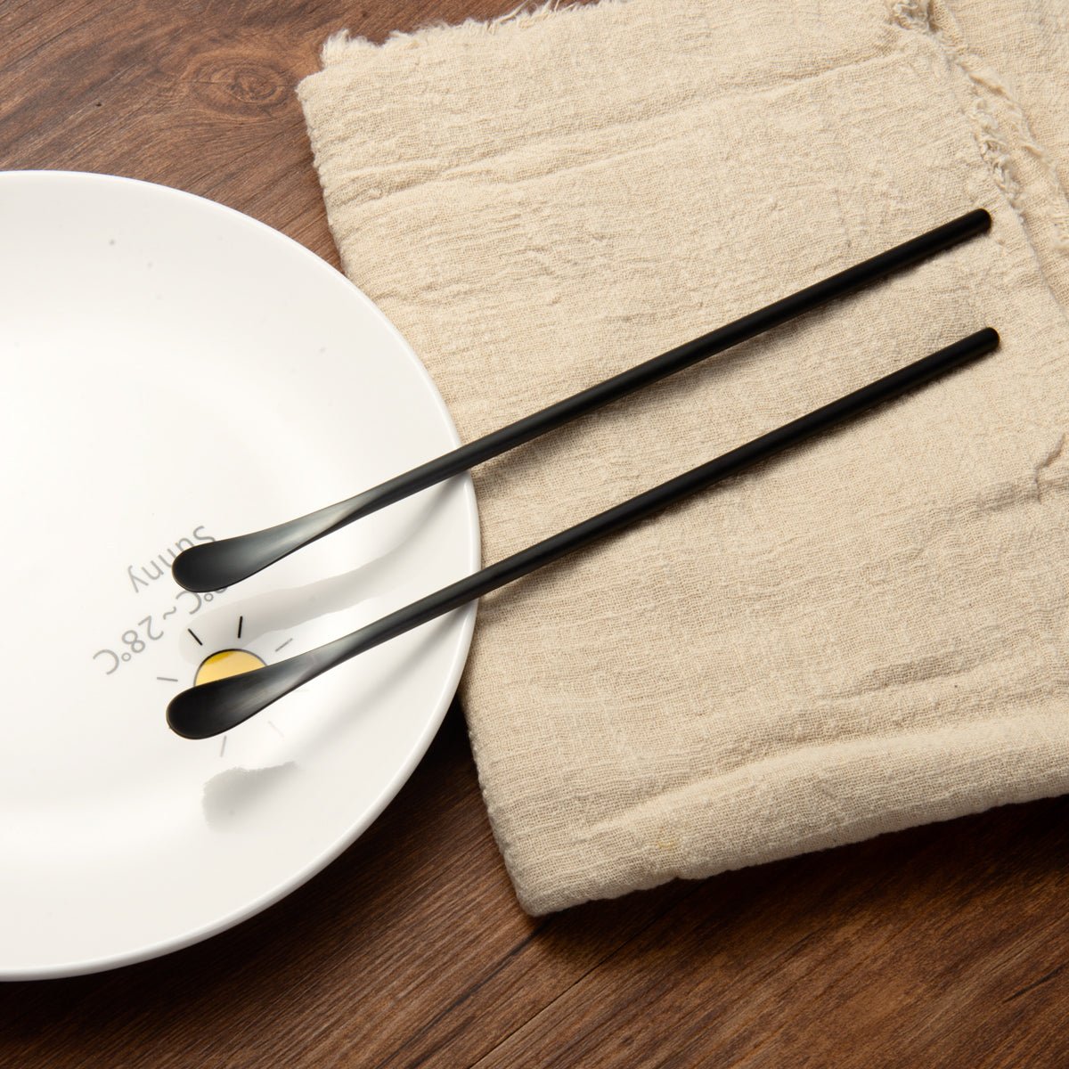 Black Stainless Steel Long Handled Teaspoon resting beside a plate for table setting