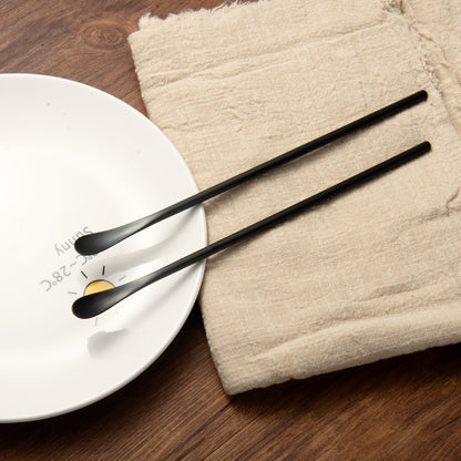 Black Stainless Steel Long Handled Teaspoon resting beside a plate for table setting
