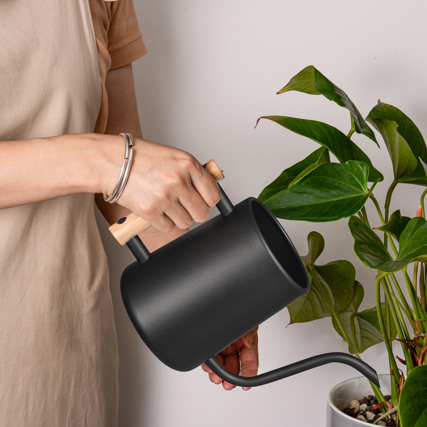Black Stainless Steel Plant Watering Pot 35oz held by hand while watering a potted plant with a long spout