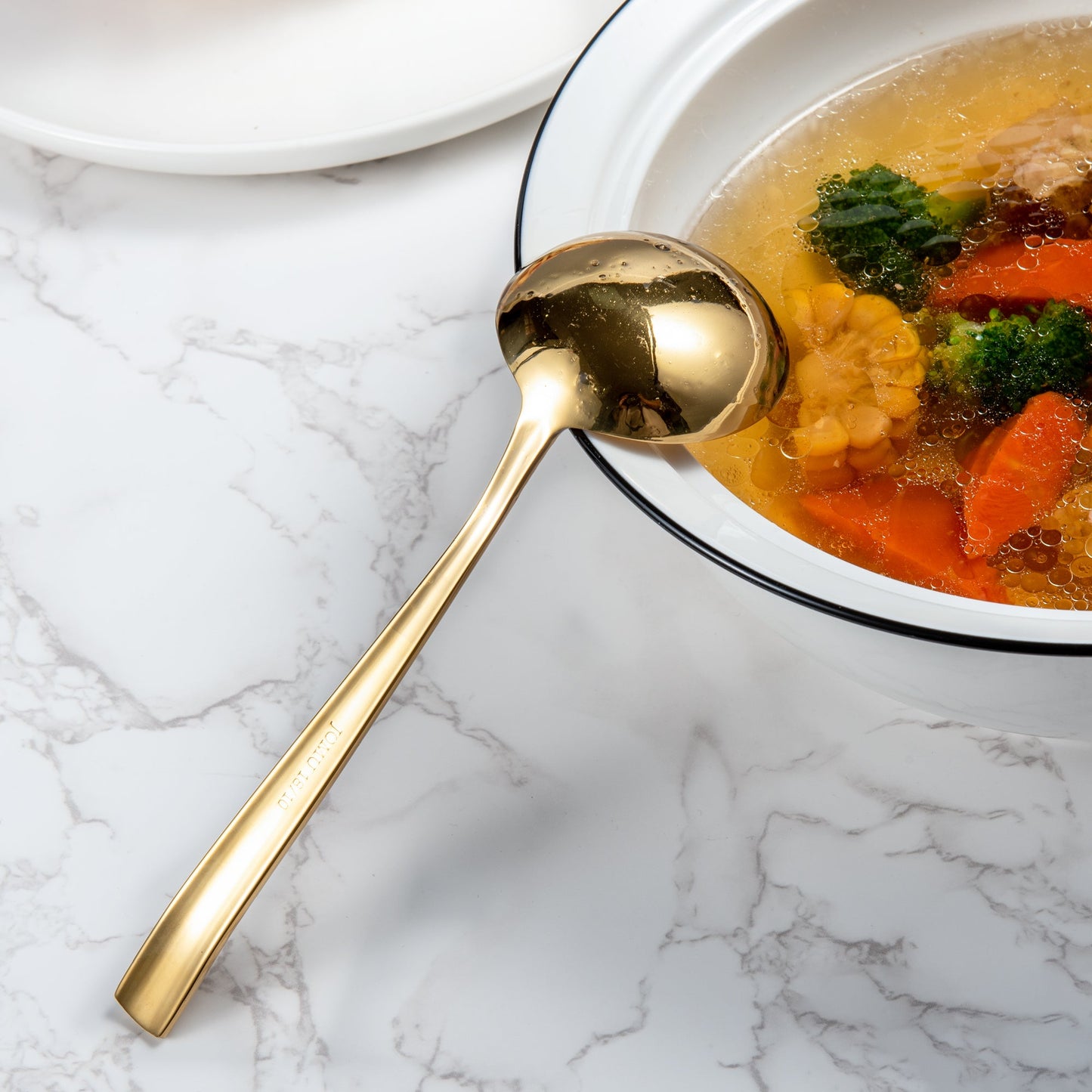 IMEEA gold stainless steel sauce ladle placed on the edge of a soup bowl