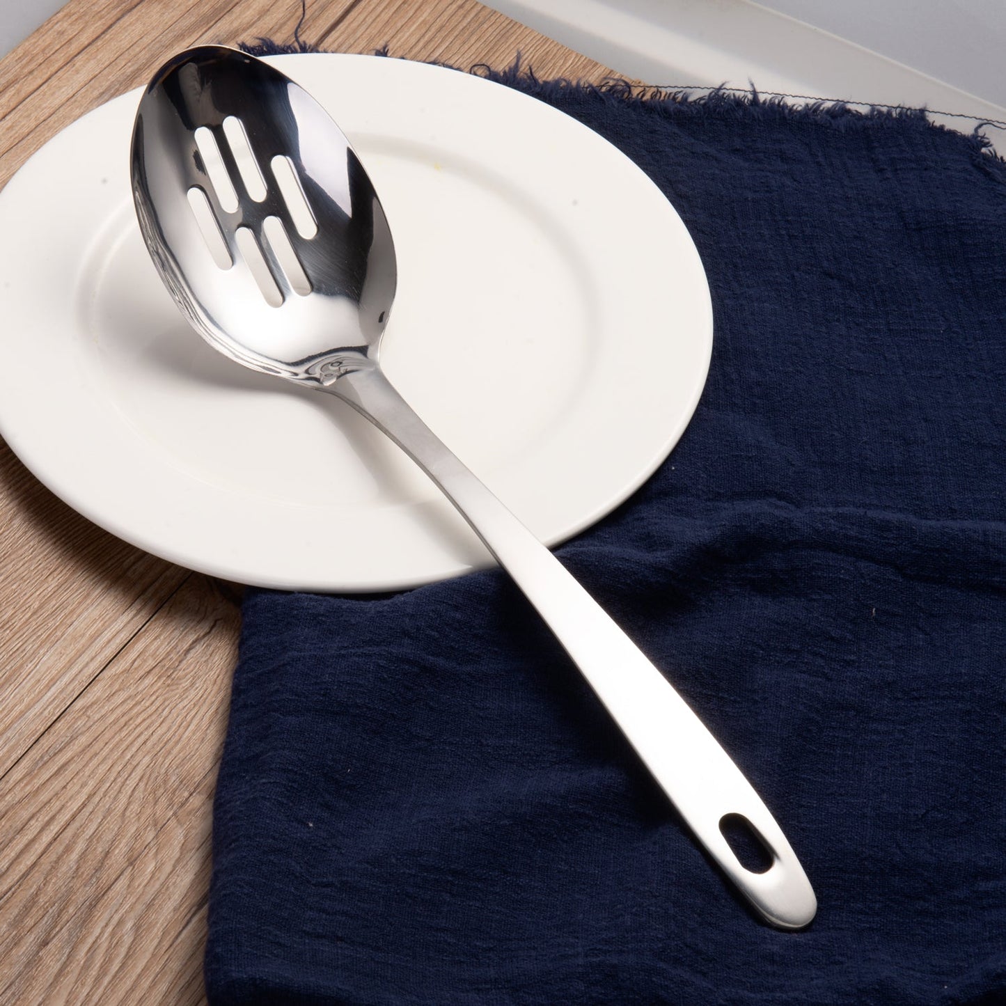 Sllotted serving spoon displayed on a dining plate with a mirror polished finish for elegant food serving