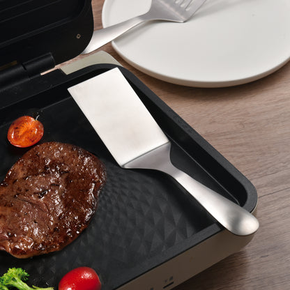 Flat Edge Stainless Steel Solid Spatula on a steak frying pan for everyday cooking tasks