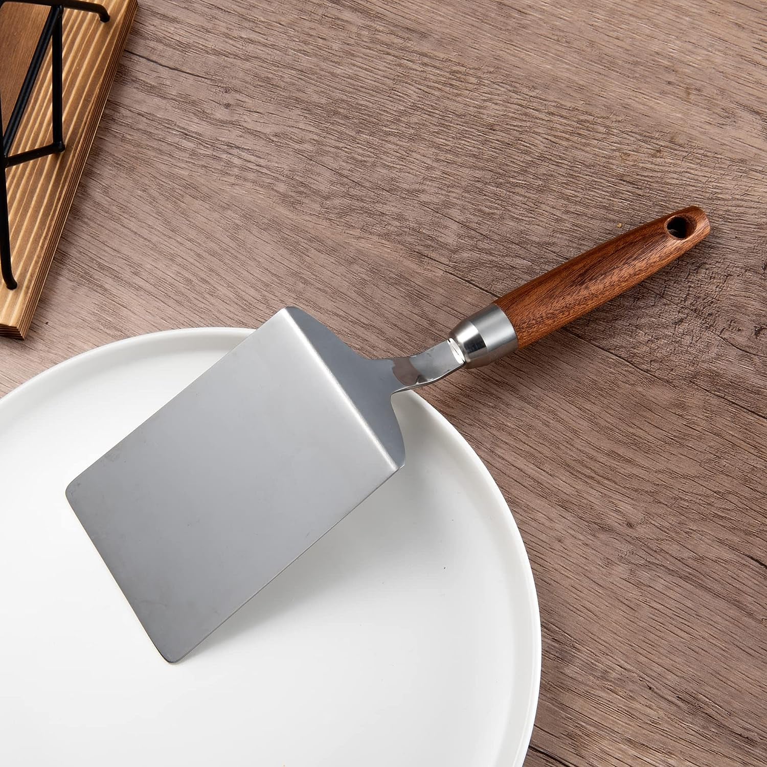 IMEEA Stainless Steel Turner Spatula with Wood Handle placed on the edge of a plate